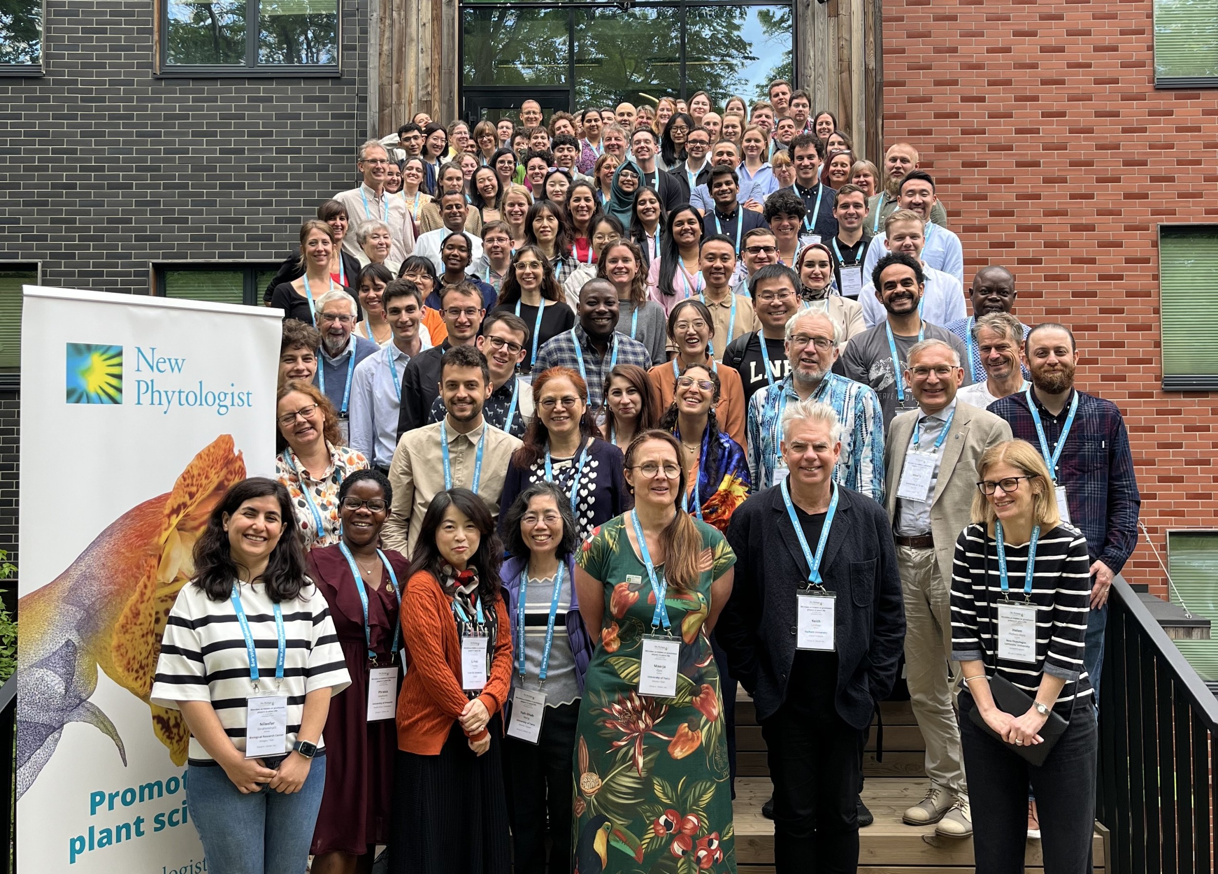 A group of around 100 symposium delegates stood on stairs outside the Oecologicum building. A New Phytologist banner is in the lower left of the photo.