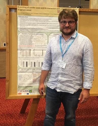 Poster prize winner Jan Lyczakowski smiling and standing next to the winning poster hung up.