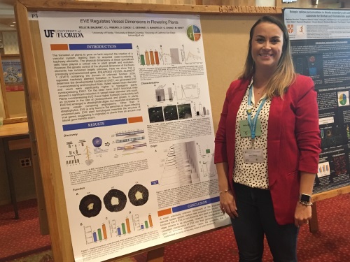 Poster prize runner-up Kelly Balmant smiling and standing next to the runner-up poster hung up.