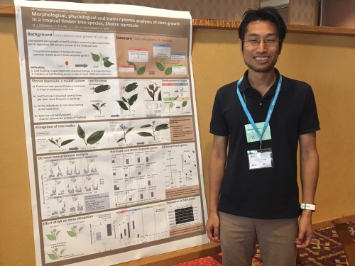 Poster prize runner-up Masaki Kobayashi smiling and standing next to the runner-up poster hung up.