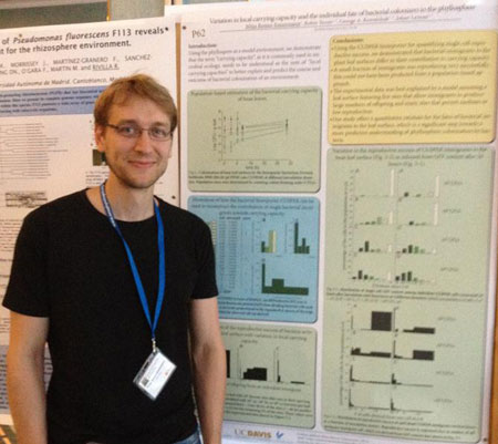 Poster prize winner Mitja Remus-Emsermann smiling and standing next to the winning poster hung up.