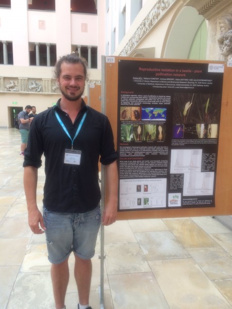Poster prize runner-up Florian Etl smiling and standing in front of the runner-up poster hung on a board.