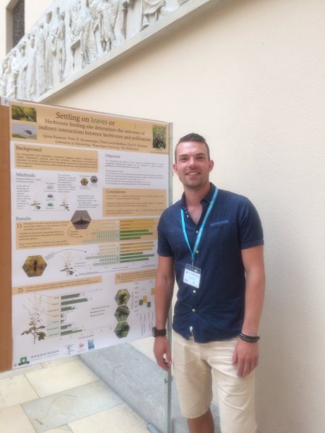Poster prize winner Quint Rusman smiling and standing in front of the winning poster hung on a board.