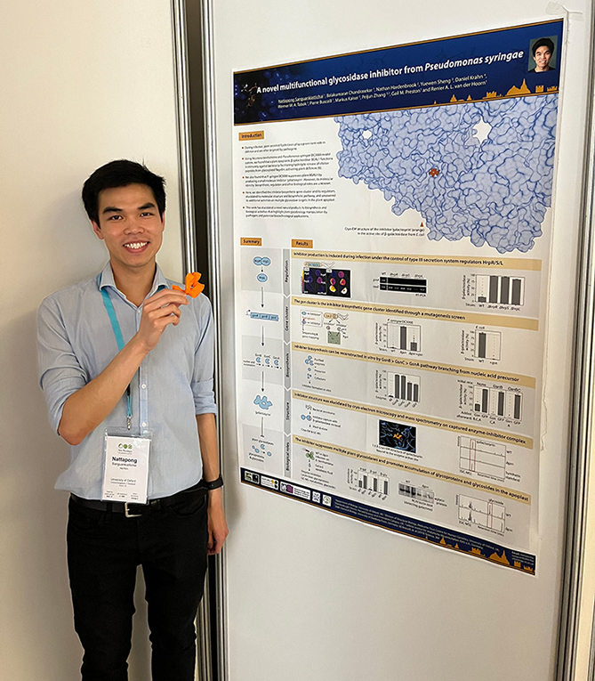 Poster prize runner-up Nattapong Sanguankiattichai smiling and standing in front of the runner-up poster mounted on the wall.
