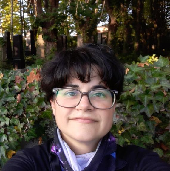 Photo of Celia rodrigues, a women wearing glasses with short hair standing in front of wall of ivy, and trees