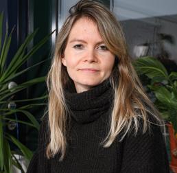Charlotte Grossiard in a black turtleneck standing in front of some house plants