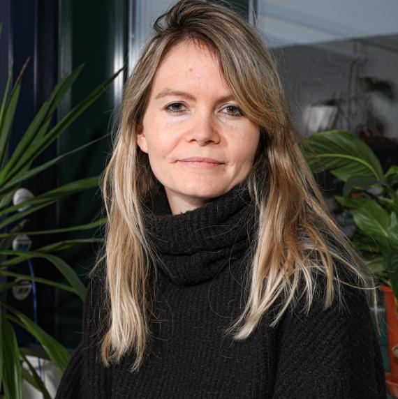 Charlotte Grossiard in a black turtleneck standing in front of some house plants