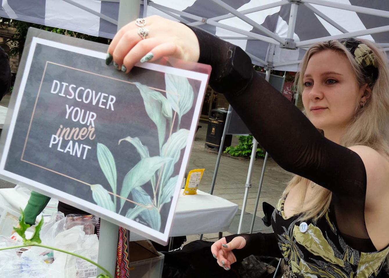 A woman holds a sign that reads 'Discover your inner plant.'