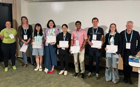 Nine people stand in a row, holding certificates