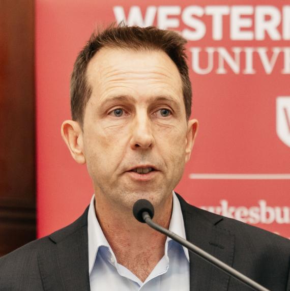 Distinguished Professor Ian Wright wearing a black blazer speaking into a microphone infront of a red sign at Western Sydney University