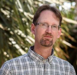 Photo of Kevin Hultine.  a man with brown hair, glasses and a beard, with a check shirt.