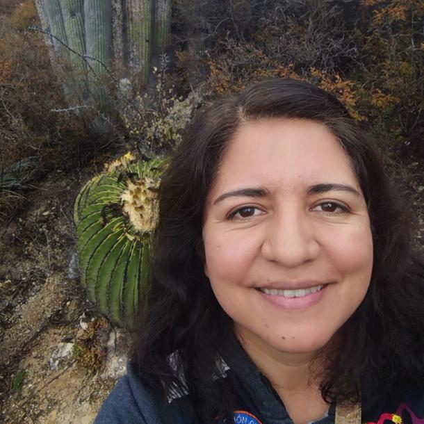 A selfie of Liliana López-Olmedo, taken amid scrubby vegetation with cacti in the background.