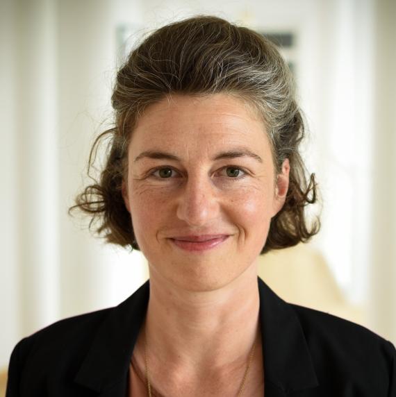 Lisa Hülsmann in a black jacket standing in a white corridor.