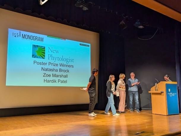 Photo of the three New Phytologist Foundation poster prize winners on stage at the Monogram 2026 conference with session chairs Kostya Kanyuka and Elizabete Carmo-Silva.