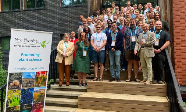 Group photo of delegates standing on steps outside a building at the 2026 New Phytologist Editor-in-Chief Symposium. A stand-up banner in the foreground reads 'Promoting plant science' and includes a selection of journal covers.