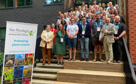 Group photo of delegates standing on steps outside a building at the 2026 New Phytologist Editor-in-Chief Symposium. A stand-up banner in the foreground reads 'Promoting plant science' and includes a selection of journal covers.