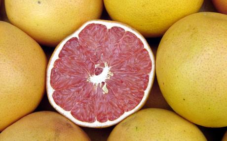 Several grapefruit, one of which has been cut open, displaying the red segments inside.