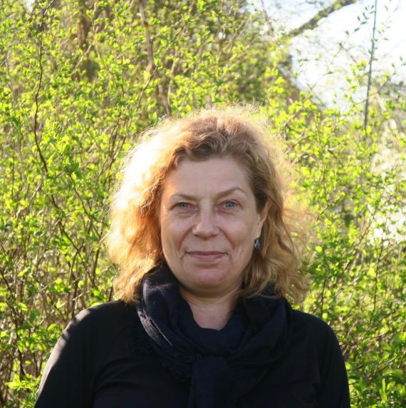 Maria E. Eriksson wearing a black coat, stood in front of bushes