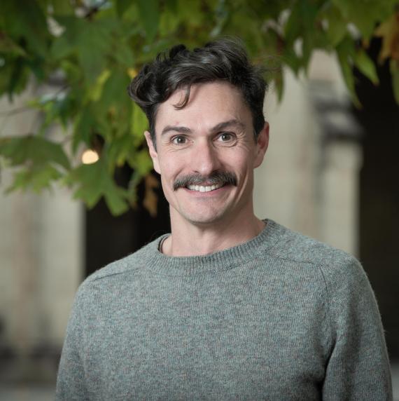 Mike Haydon wearing a grey jumper stood in front of a leafy background