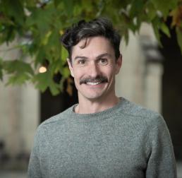 Mike Haydon wearing a grey jumper stood in front of a leafy background