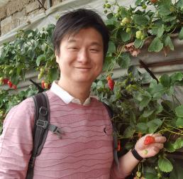 Wei  Wang wearing a pink jumper, holding a strawberry on a strawberry bush