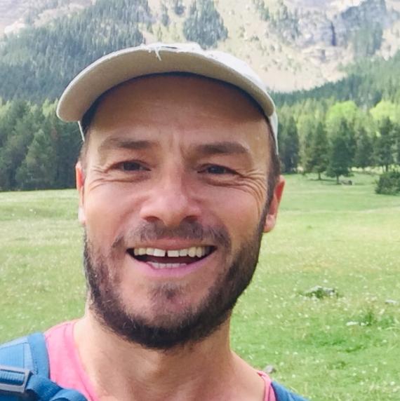 Rob Ingle stood in a grassy field, with hills and forest in the background