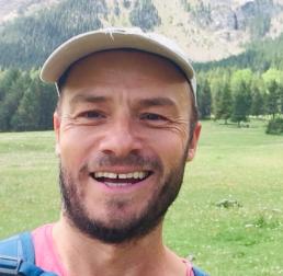 Rob Ingle stood in a grassy field, with hills and forest in the background