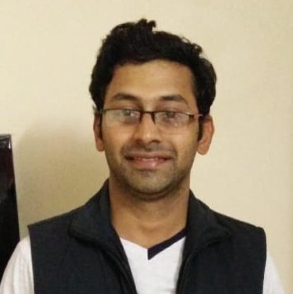 Amey Bhide wearing a white t-shirt and black jumper, in front of a plain cream background