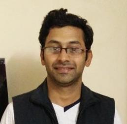 Amey Bhide wearing a white t-shirt and black jumper, in front of a plain cream background