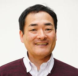 Norihito Nakamichi wearing a white shirt and red jumper, in front of a white background
