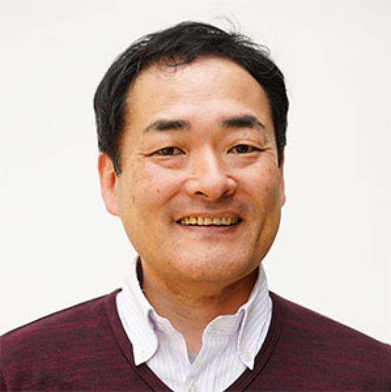 Norihito Nakamichi wearing a white shirt and red jumper, in front of a white background
