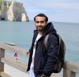 Ravi Suresh Devani stood on a walkway above a beach, with cliffs in the background