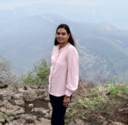 Arati Vasav wearing a pink shirt, stood outdoors with mountains in the background