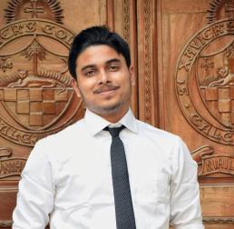 Kankan Datta wearing a shirt and tie, stood infront of a wooden background with crests