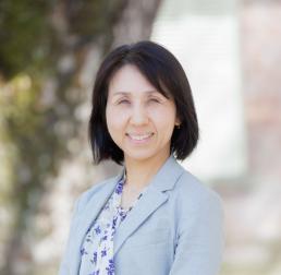 Akiko Satake wearing a light blue suit, stood in front of a tree