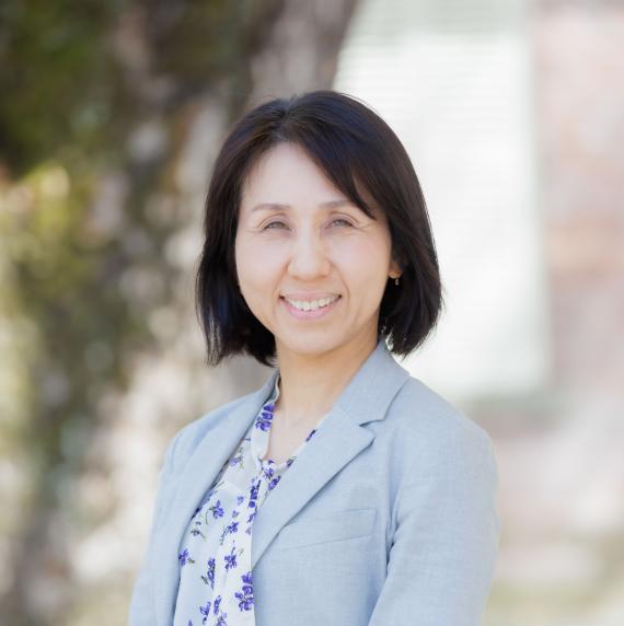 Akiko Satake wearing a light blue suit, stood in front of a tree