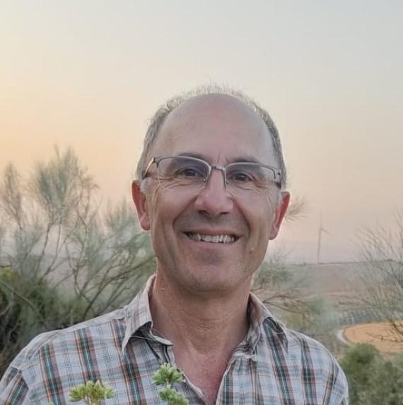 Photo of Rafael Villar, a man with glasses with a pine tree/bush in the foreground and fields in the background