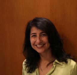 Photo of Renata Libonati, a smiling women with dark hair standing in front of wood panelling
