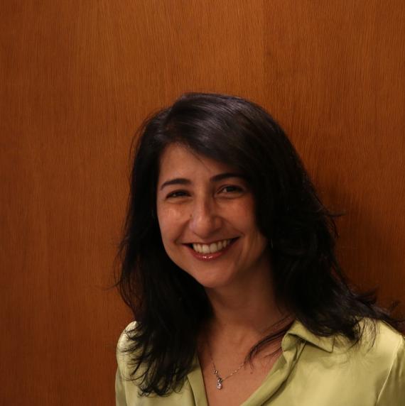 Photo of Renata Libonati, a smiling women with dark hair standing in front of wood panelling