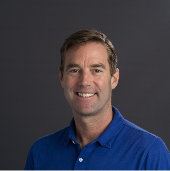 Josh Gendron wearing a blue polo smiling, in front of a dark grey background