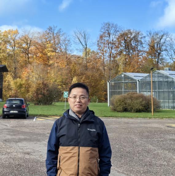 Zhilin Yuan standing in front of a greenhouse with a forest in the background