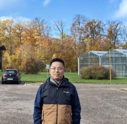 Zhilin Yuan standing in front of a greenhouse with a forest in the background