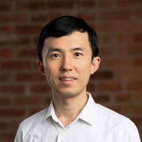 Kai Zhu, wearing a white shirt in front of a red brick wall
